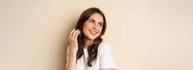 Close up portrait of coquettish beautiful girl gazing silly, gently smiling and giggling, posing flirty and cute against beige background. Women beauty and valentines concept.