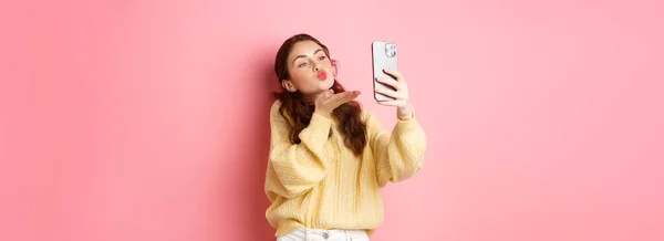 漂亮的调情女孩在智能手机上自拍 在视频聊天的过程中 在粉色背景下亲吻自己 复制空间 — 图库照片