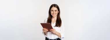 Portrait of smiling corporate woman looking at digital tablet, working, standing over white background.