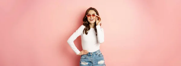 stock image Portrait of stylish glam girl in sunglasses, laughing and smiling, standing over holiday pink background. Copy space