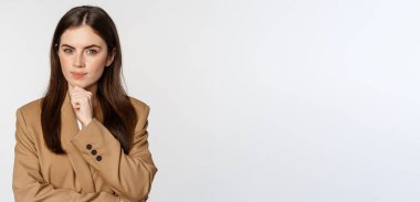 Image of businesswoman thinking, corporate woman looking thoughtful, making decision, standing in brown suit over white background.