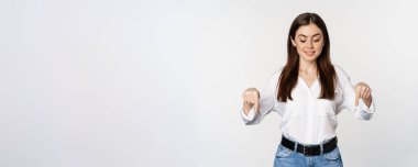 Portrait of smiling business woman pointing and looking down, showing advertisement, logo or banner below, standing over white background.