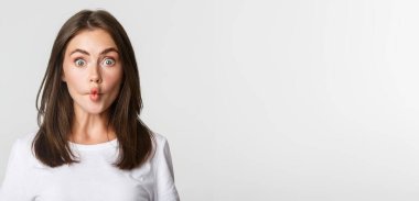 Komik ve sevimli esmer kız dudaklarını emer, balıkların yüzünü buruşturur, beyaz arka plan.