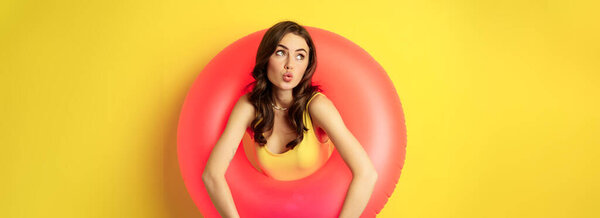 Close up portrait of coquettish young sexy woman inside pink swimming ring, concept of beach holiday, vacation and summer, yellow background.