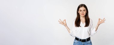 Yoga and mindfulness. Young woman meditating with closed eyes, breathing freely and showing mudra nirvana sign, standing peaceful over white background.