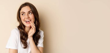 Close up portrait of coquettish beautiful girl gazing silly, gently smiling and giggling, posing flirty and cute against beige background. Women beauty and valentines concept.