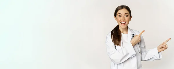 バナー広告を表示するには 右の指を指して 女性医師 驚くべき笑みを浮かべて プロモーション割引をチェックアウト 白い背景 — ストック写真