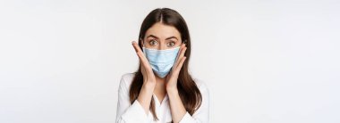 Covid-19 ve pandemik konsept. Coronavirus sosyal mesafesi sırasında tıbbi maske takan genç bir ofis kadını beyaz arka planda duruyor..