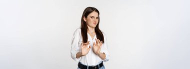 Displeased woman showing stop, rejection gesture, waving hands to decline, refuse of something ugly, standing over white background.