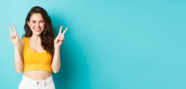 Yaz tatili ve duygu konsepti. Sevimli kız gülümseyip gülüyor, mavi arka planda barış işaretleri gösteriyor..