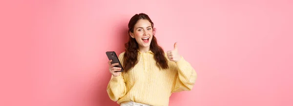 在智能手机上使用应用程序 网上购物应用程序 站在粉色背景下 面带微笑而感到满意的迷人迷人女孩的肖像 — 图库照片