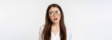 Close up of confused brunette woman in glasses, looking puzzled and clueless, standing over white background. Copy space