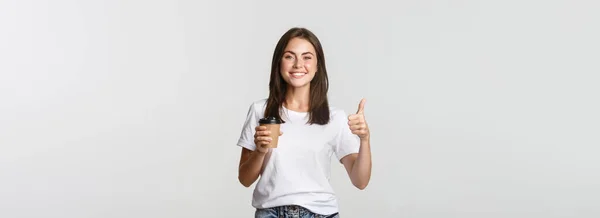 Atrakcyjny Uśmiech Brunetka Dziewczyna Patrząc Zadowolony Picie Kawy Pokazać Kciuki — Zdjęcie stockowe