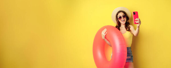 Stylish brunette girl on vacation, taking selfie with swim ring, going on beach, swimming in sea on summer holiday, standing over yellow background.