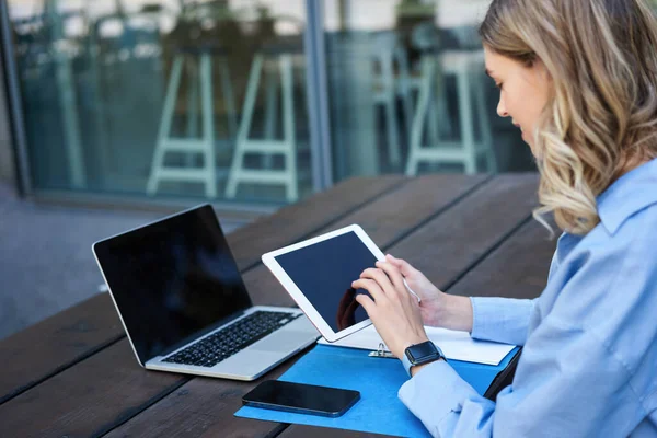 Dijital tablet üzerinde çalışan iş kadınının portresi, diyagramları kontrol etmek, ofis binasının yakınındaki açık havada oturmak. Şirket kadını iş toplantısına hazırlanıyor..