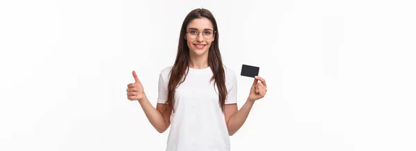 穿着T恤衫 带着自信 快乐和微笑的年轻女性的画像 大拇指翘起 点头表示同意 推荐银行 展示信用卡 用非现金在网上购物 — 图库照片