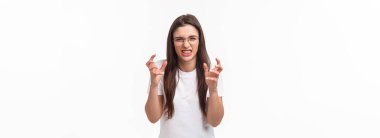 Waist-up of hateful and pissed-off, annoyed young female telling about person she hates, clench hands into fists, cursing, swearing at guy, want strangle someone from annoyance, white background.