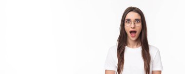Hevesli, entrika dolu, genç esmer kadının yakın plan portresi. İnanılmaz haberlere kulak veren, ağzı açık, büyülenmiş, ayakta duran beyaz arka plan, harika bir fikir, gözlük takıyor..
