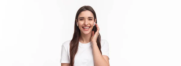 魅力的な笑顔の幸せな女性のクローズアップ肖像画 ワイヤレスヘッドフォンに触れる 友人に連絡するイヤホンを使用して イヤホンと電話で会話をします 屈託のない笑い — ストック写真