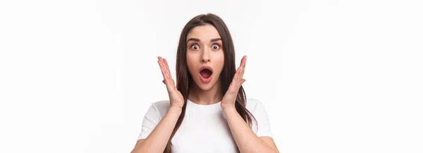 What an amazing news. Surprised and astonished, excited young woman react to something awesome happened, gasping, open mouth and raise hands near face, staring camera, white background.