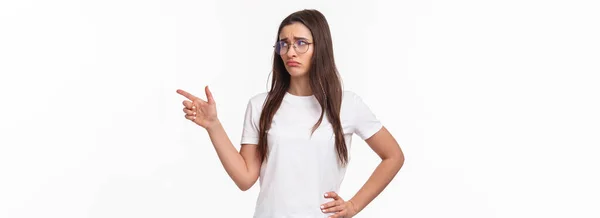 ウエストアップポートレートの不安 悲しいと悲観的な若いブルネットの女性でメガネ 探していると指を指して右に吸い込ま不幸な顔で 嫉妬や後悔を表現します 悲しみ白の背景 — ストック写真