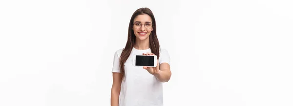 コミュニケーション テクノロジー ライフスタイルの概念 メガネやTシャツを着た若い魅力的な女性の肖像画 スマートフォンの画面を水平表示し ゲームやアプリケーションを紹介します — ストック写真