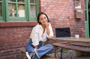Laptoplu güzel Asyalı kadın, kafede oturuyor ve çalışıyor, gülüyor ve gülümsüyor, kahve içiyor. Kentsel yaşam tarzı ve insanların konsepti