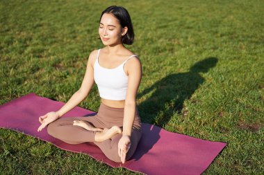 Gülümseyen Asyalı kadının portresi meditasyon yapıyor, temiz havada yoga yapıyor, lastik minderde dinleniyor, parkta egzersiz yapıyor, hava soluyor, sakin oluyor..