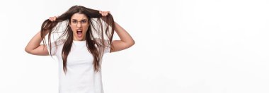 Waist-up portrait of bothered and annoyed, angry pissed-off young girlfriend losing temper, pulling hair from head and screaming being furious and outraged, white background.