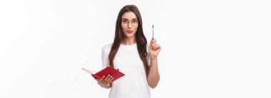 Yaratıcı hevesli genç bayanın harika bir fikri var, not defterine unutmamak için, kalemini Eureka işareti ile yükseltmek, heyecanla gülümsemek, hazırlık planı veya günlük program, beyaz arka plan.