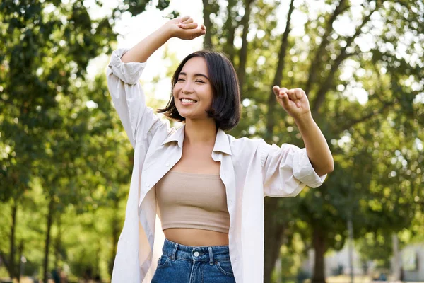 stock image Carefree woman dancing and walking in park with hands lifted up high, smiling happily. Lifestyle concept.