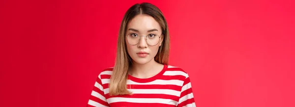 特写镜头严肃 重点突出的聪明的亚裔女学生仔细听讲座 看相机聚精会神地戴着规定的眼镜站在条纹T恤红色背景上 复制空间 — 图库照片