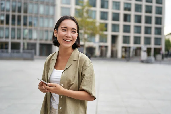 市の広場に立って 携帯電話を保持するアジアの女性の肖像画 屋外でスマートフォンを歩く女の子 — ストック写真