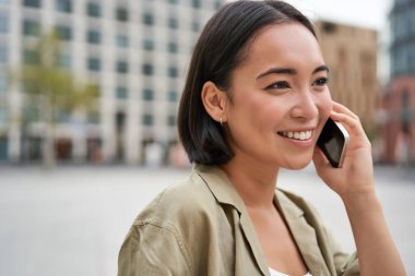 Modern Asyalı genç kız cep telefonuyla konuşuyor, şehir caddesinde telefon kullanıyor. Akıllı telefondan birini ararken gülümseyen bir kadın..