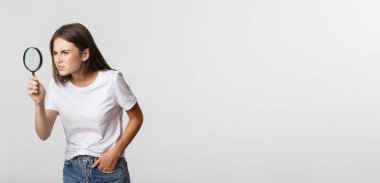 Ciddi görünümlü çekici bir genç kadın bir şey arıyor, büyüteçten bakıyor, beyaz arka plan..