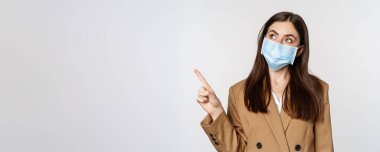 Coronavirus ve insanlar konsepti. İş yerindeki yüz maskesi takan iş kadını portresi logoyu işaret ediyor, şirket afişi, beyaz arka plan..