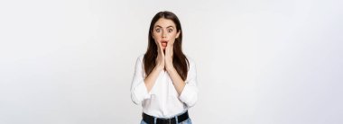 Surprised brunette woman looking amazed, seeing smth awesome, standing in blouse and jeans over white background.