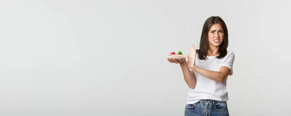 stock image Disgusted young woman rejecting eating awful cake, making refusal gesture and grimacing displeased.