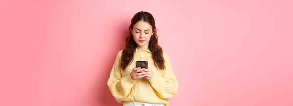 年轻的微笑女人在社交媒体上聊天 在智能手机上读信息 站在粉红的背景下 — 图库照片