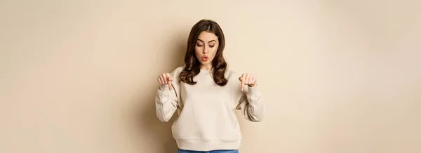 Surprised Girl Pointing Looking Smth Curious Beige Background — Foto de Stock