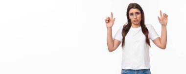 Sıkıntılı, üzgün ve kasvetli, t-shirt ve gözlüklü genç esmer kadının belden aşağısı portresi, parmaklarını silkip sefil, huzursuz bir yüz ifadesi takınıyor, karar veremiyorum..