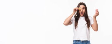 Kızın portresi açık ağızla kameraya şaşkın şaşkın bakıyor, hayret verici ve muhteşem bir şeye bakıyor, gözünün üstüne makarna koyuyor, beyaz arka planda duruyor, lezzetli tatlılar ile harika bir kafe buluyor..