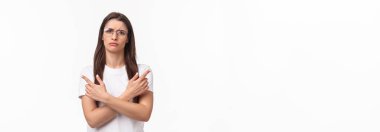 Kararsız, şaşkın ve kafası karışmış gözlüklü, tişörtlü, çapraz elli, iki farklı türü işaret eden, kaşlarını çatan, karar veremeyen, beyaz arka planlı güzel bir kadının belden yukarı portresi..