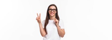 Eğlence, eğlence ve tatil konsepti. Tasasız, neşeli genç kızın portresi harika bir parti veriyor, barış işaretini kutluyor, karnaval maskesi takıyor, beyaz arka planda duruyor..