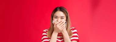 Yakın plan, sevimli, aptal Asyalı kız kıkırdıyor, eğleniyor, palmiye dudakları basıyor, sır vermeyeceğine söz veriyor, gülüyor, arkadaşça gülüyor, kırmızı arka planda sırıtıyor..