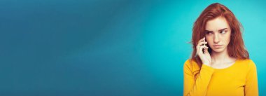 Yaşam tarzı kavramı - Kızıl kızıl saçlı kız arkadaşı ile cep telefonuyla konuşurken şok edici ve stresli ifade ile portresi. Pastel mavi arka plan üzerinde izole. Kopya alanı.