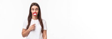 Eğlence, eğlence ve tatil konsepti. İlk Nisan 'da komik ve neşeli bir kutlama günü portresi, eğlenmek, büyük dişli ve dudaklı sopa tutmak, komik suratlar göstermek, beyaz arka plan.