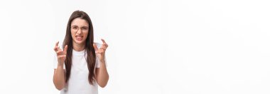 Waist-up of hateful and pissed-off, annoyed young female telling about person she hates, clench hands into fists, cursing, swearing at guy, want strangle someone from annoyance, white background.