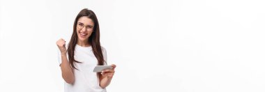 İletişim, teknoloji ve yaşam tarzı kavramı. Başarılı, neşeli, şanslı bir kızın oyunda kazandığı ödülün portresi, sert bir şekilde bitirilmiş, cep telefonu uygulamasında kazandıktan sonra yumruk yumruğa, beyaz arka plan.