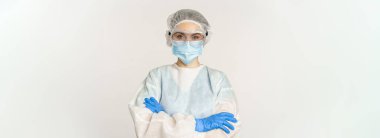Professional doctor in personal protective equipment from coronavirus, cross arms on chest, looking confident, standing over white background.
